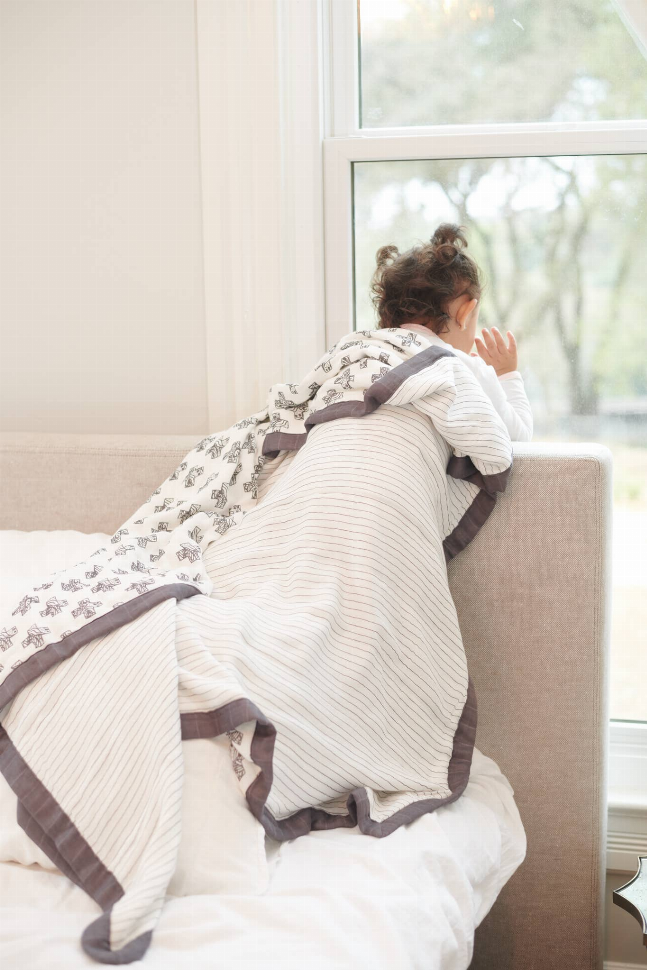 Light striped throw blanket with dark border and Nordic cross pattern, draped on bed