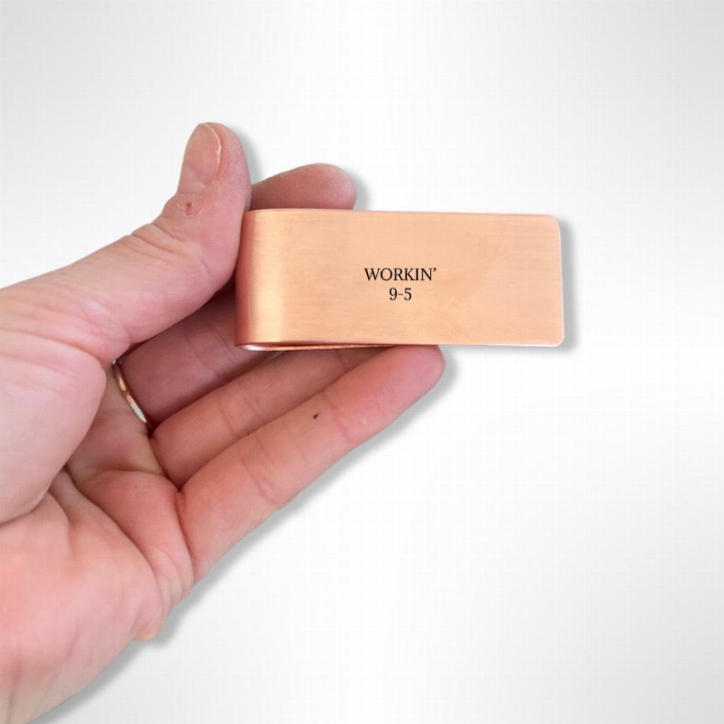 Copper-tone money clip held in hand, 'WORKIN 9-5'