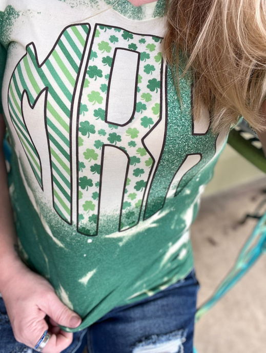 Close-up green bleached monogram tee with clover-pattern letter and stripes