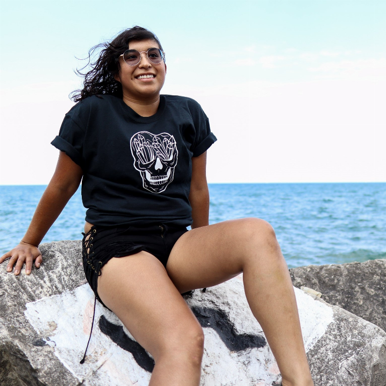 Black crew-neck T-shirt with white skull print on chest, seated model