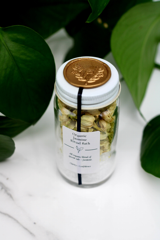 Bath salt jar with gold lid, white label, and clear contents with dried flowers