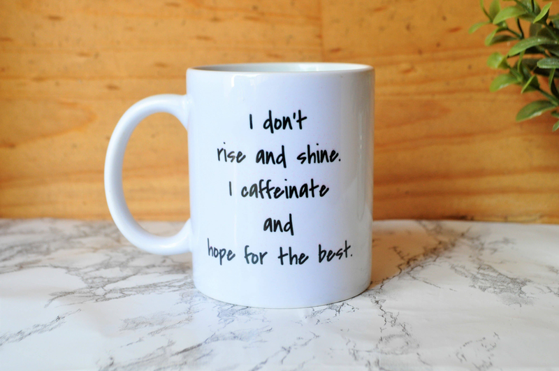 White coffee mug with black quote: 'I don't rise and shine' and 'hope for the best'
