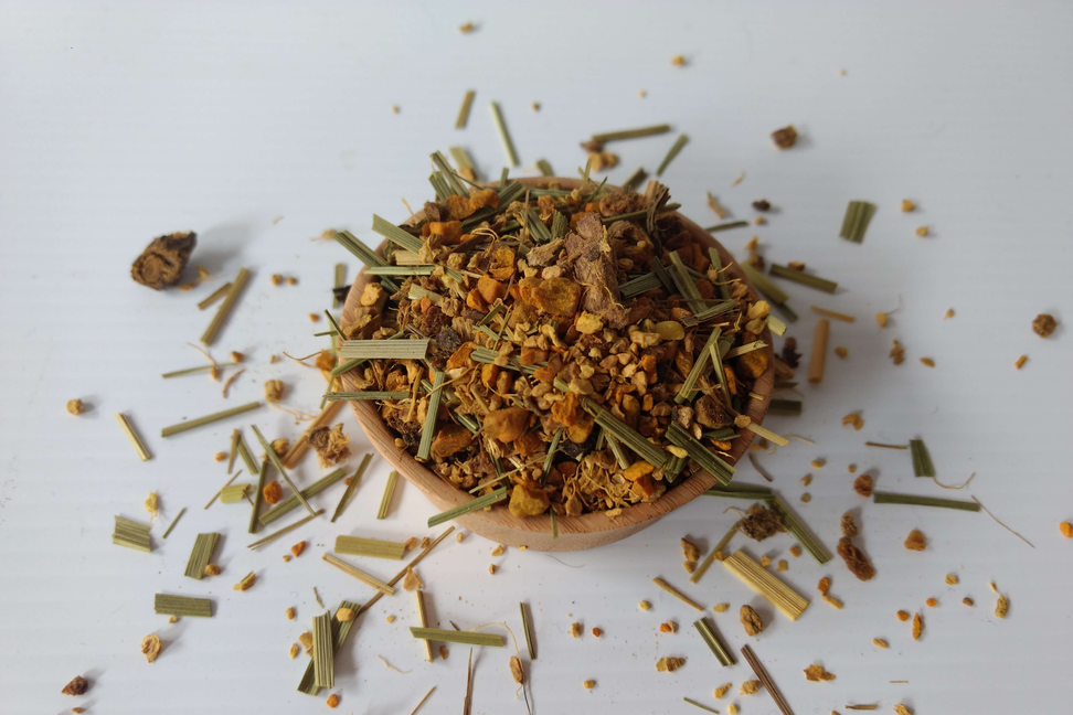 Turmeric ginger tea blend in a small bowl with yellow-orange and green herb pieces