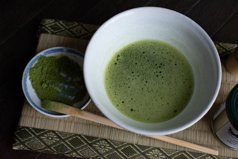 Bowl of whisked green matcha tea with wooden bamboo whisk and scoop
