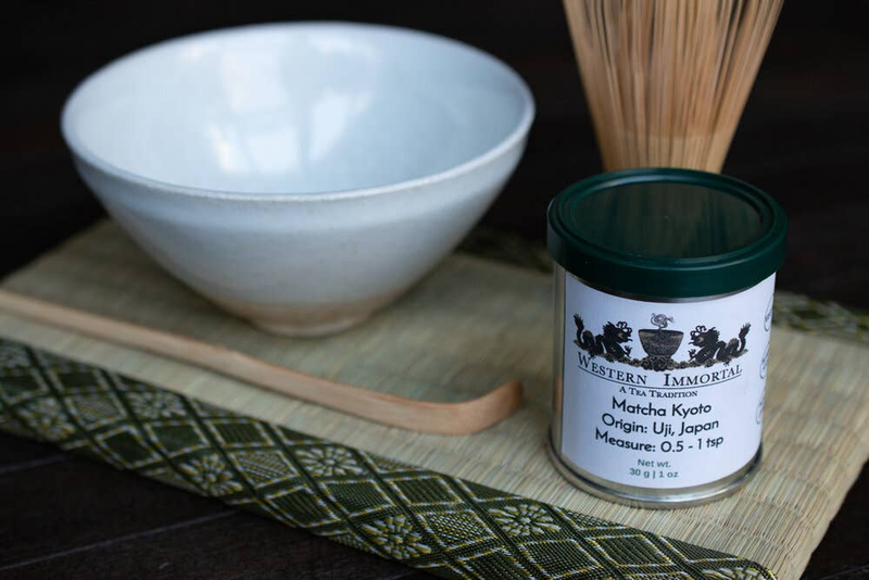 Matcha tea jar beside white bowl and bamboo tea whisk