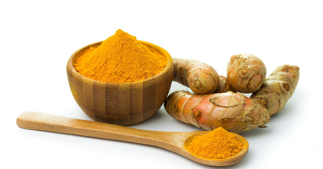 Turmeric facial mist ingredients: turmeric powder in bowl with fresh roots and wooden spoon