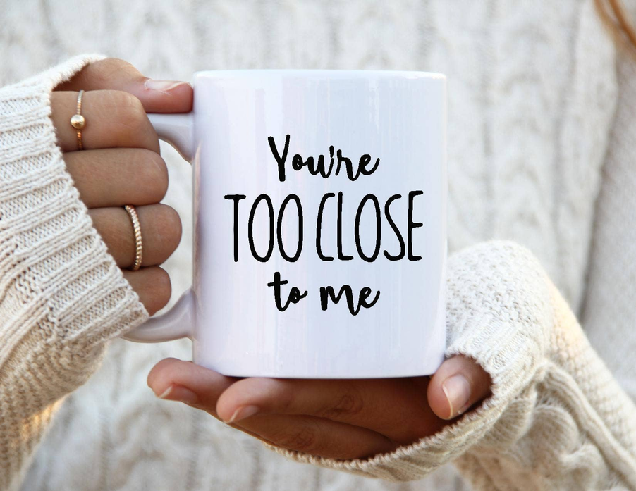 White coffee mug held in hands, 'You're too close to me' printed in black
