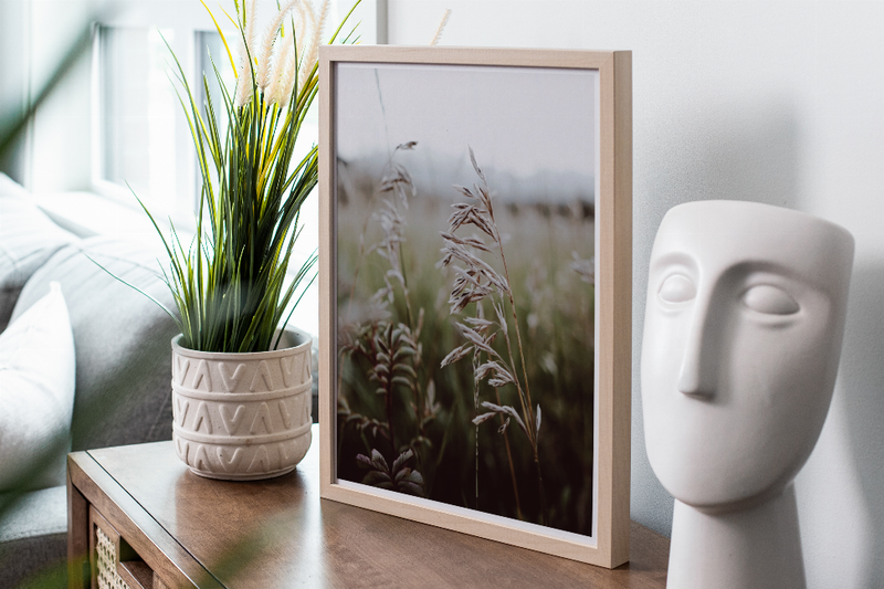 Wood-framed plant field photo print with beige grasses on a console table
