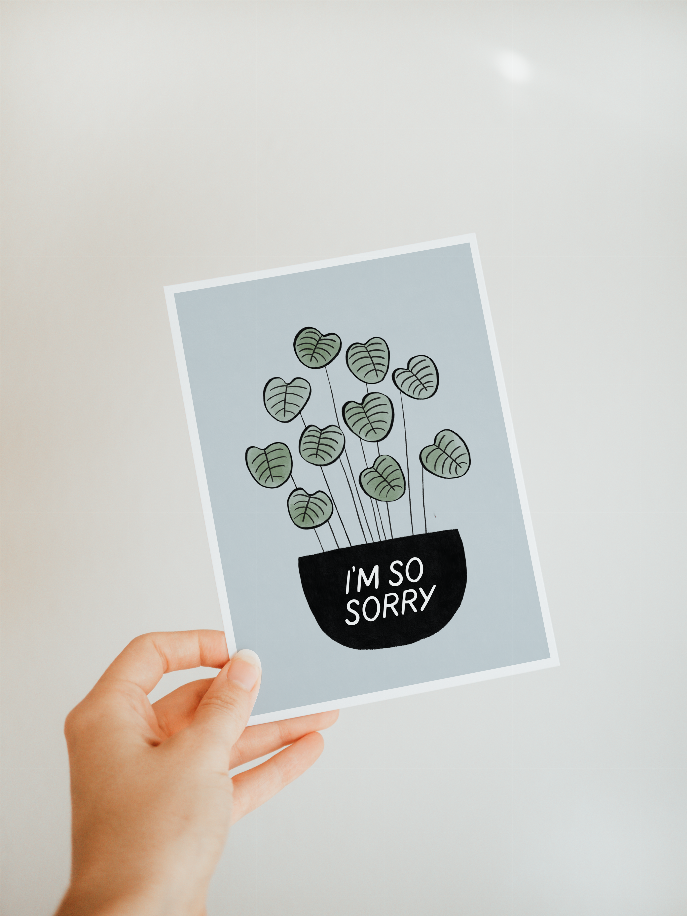 Hand holding a greeting card with green leaf doodles and 'I'm so sorry' black text