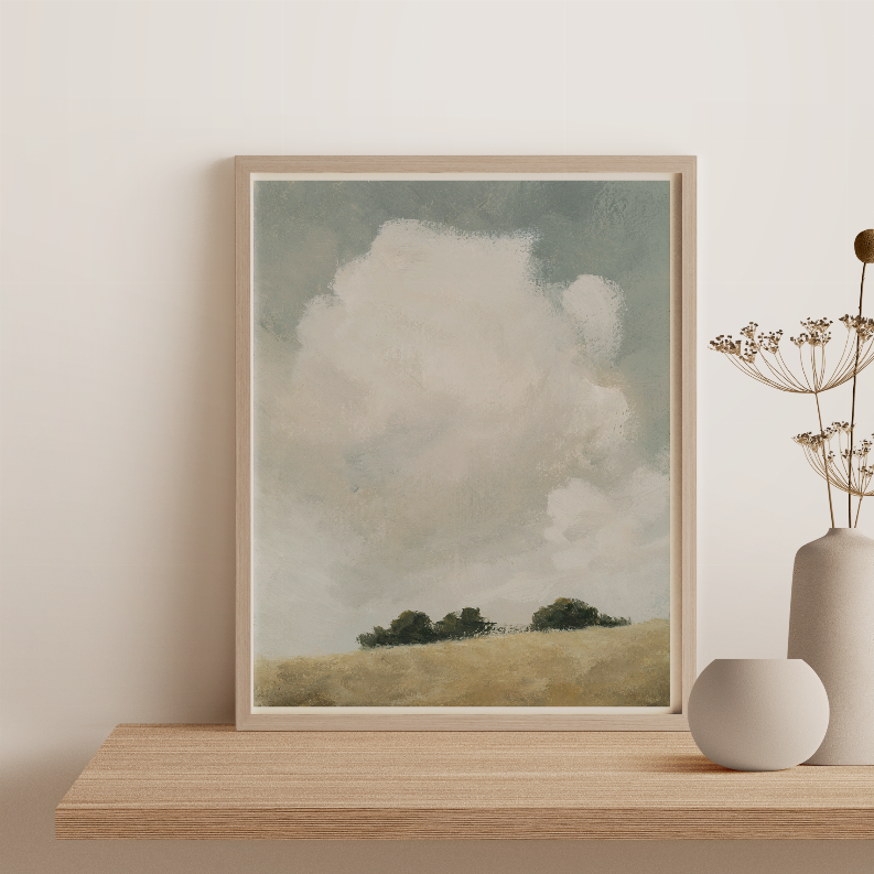 Wood framed landscape print with cloudy sky, green trees, and beige hill