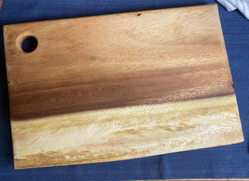 Live edge square wood cutting board with round hanging hole, warm natural grain.