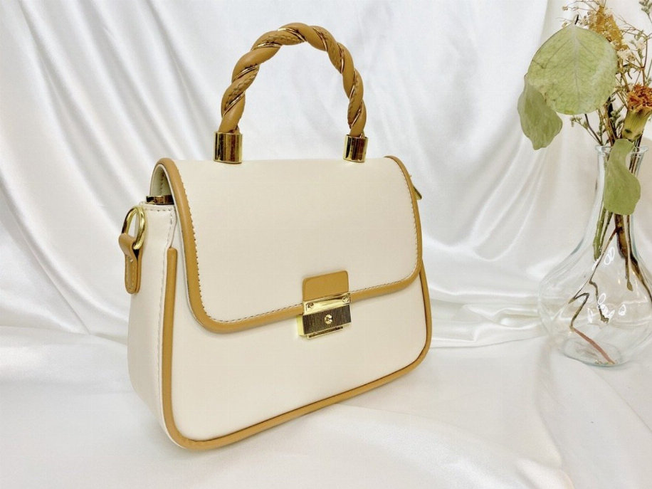 Cream small handbag with braided top handle, gold lock closure, and short side pull tab.