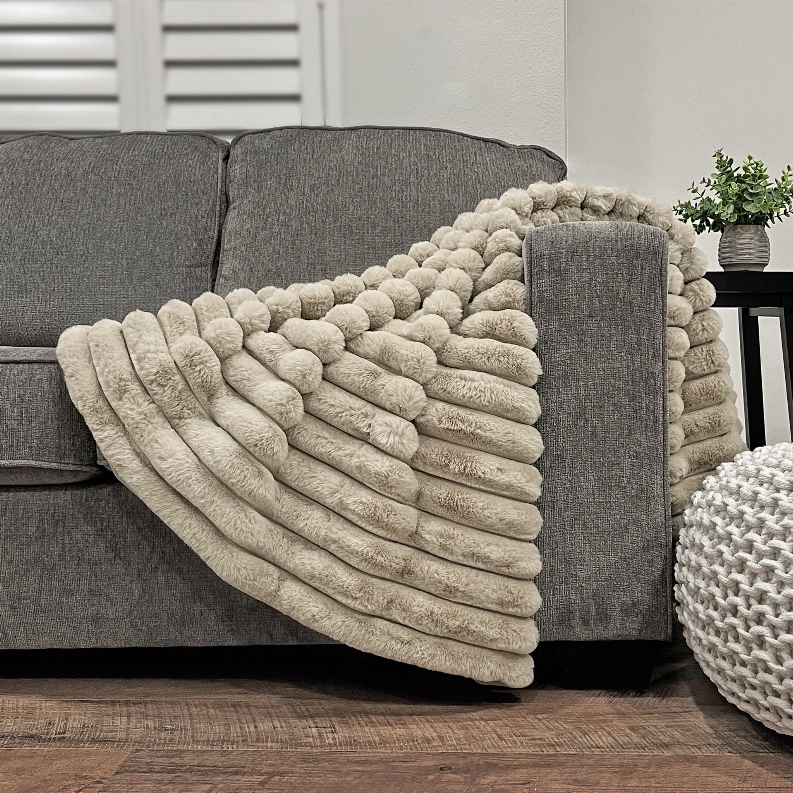 Puffy faux fur throw blanket, light beige draped over sofa with fluffy ridged surface