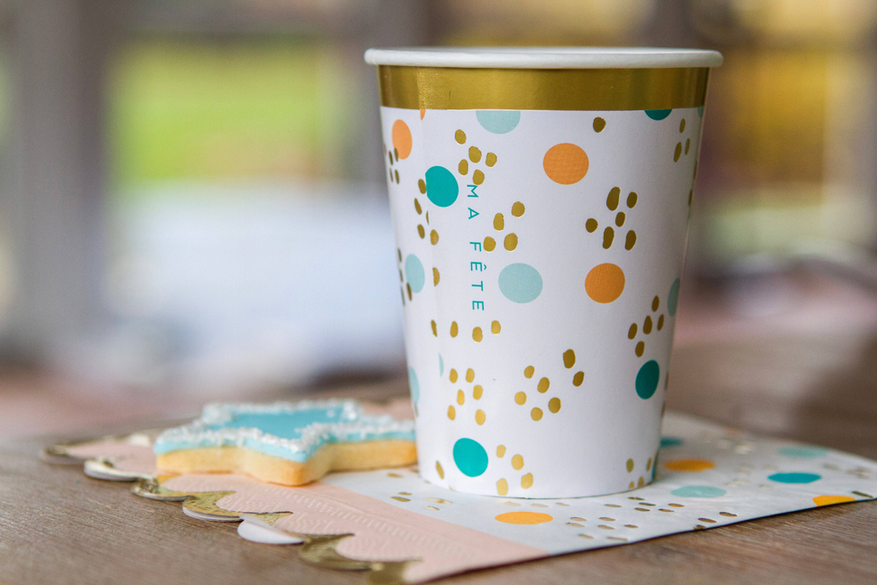 Fun fair paper cup with gold rim and colorful dot and paw-print design on tabletop
