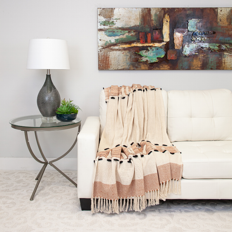 Woven rectangle throw blanket draped on sofa, cream and terracotta with fringe border