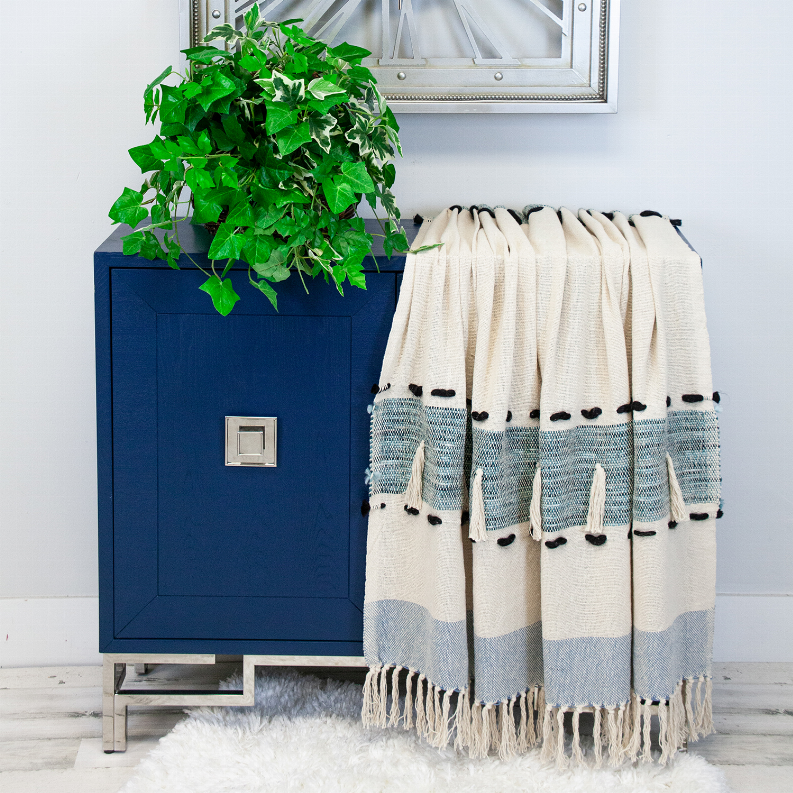 Rectangle throw blanket in cream and light-blue blocks, fringed hem with black tassels.