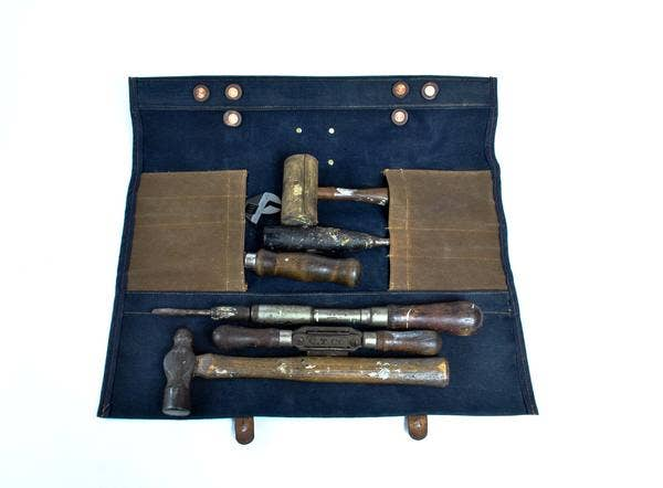 Blue tool roll holding assorted hand tools in interior compartments, leather straps