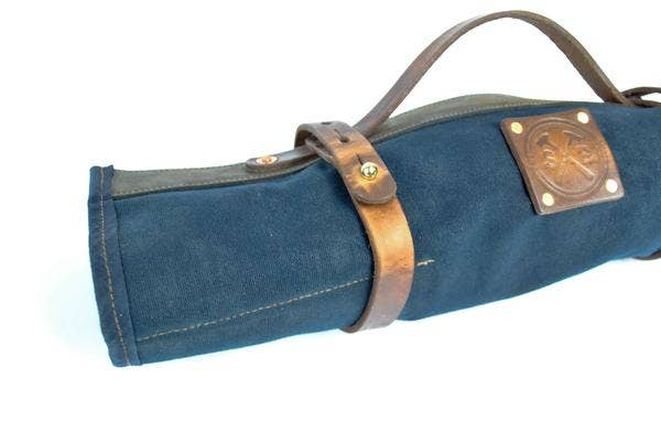 Rolled blue tool roll with brown leather handle straps and embossed front patch