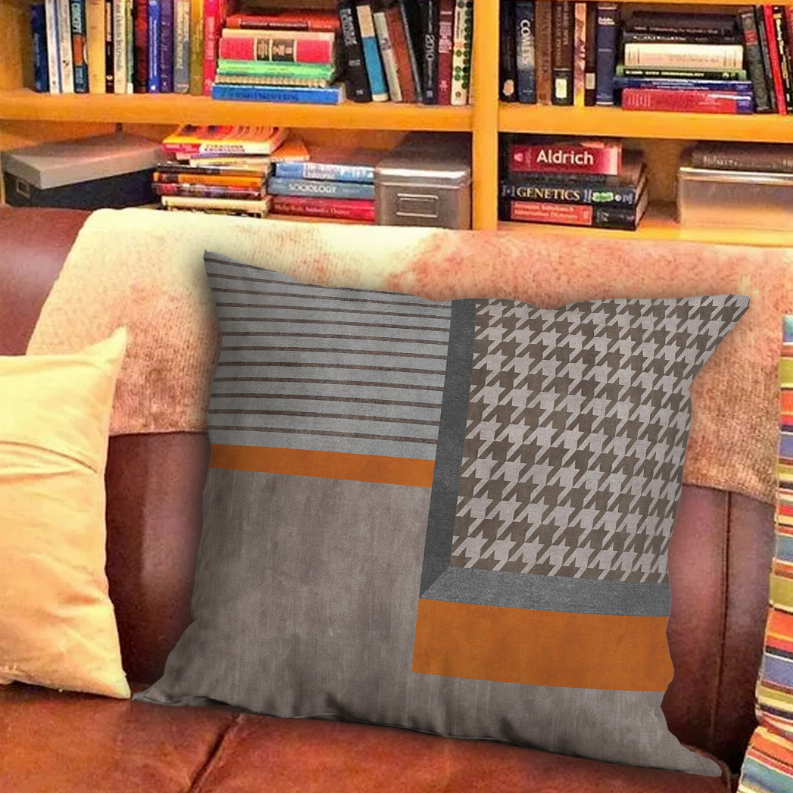 Gray patchwork decorative pillow with orange stripe accents and houndstooth section