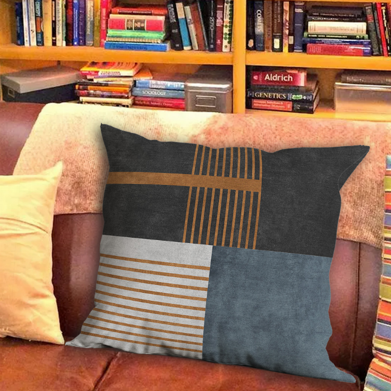 Patchwork throw pillow with dark gray geometric panels, tan striped section, blue-gray backing