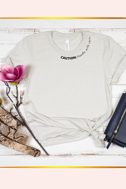 Light gray short-sleeve crewneck T-shirt with 'CAUTION: Handle with care' print
