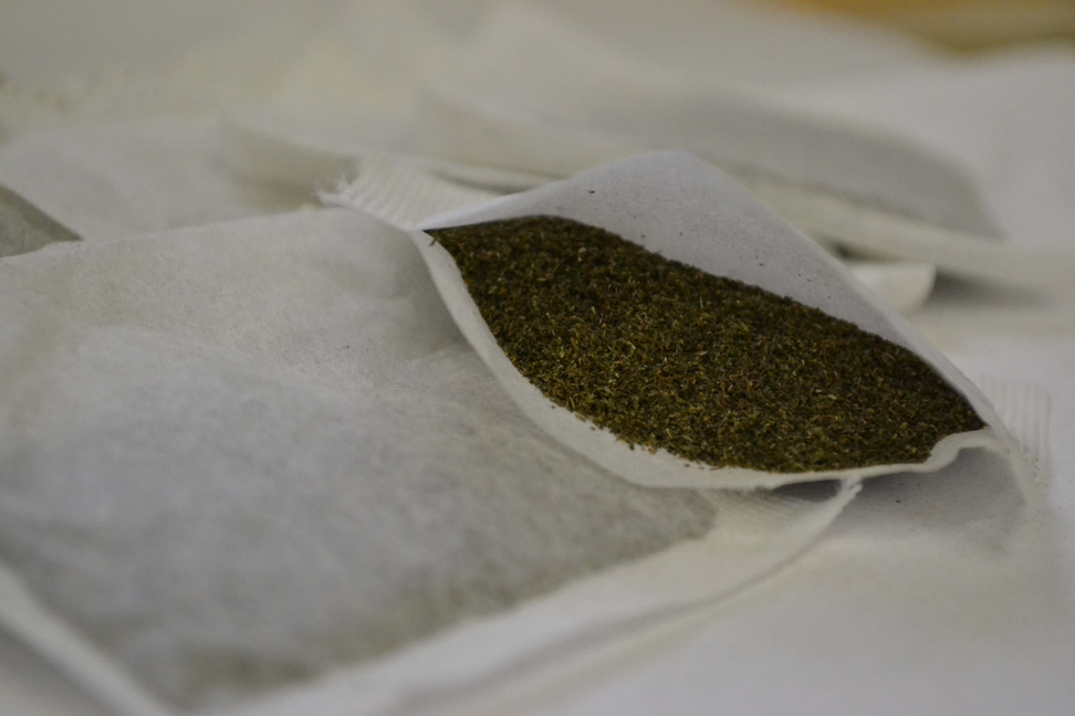 Spearmint tea bag with green tea granules inside, open pouch and string visible