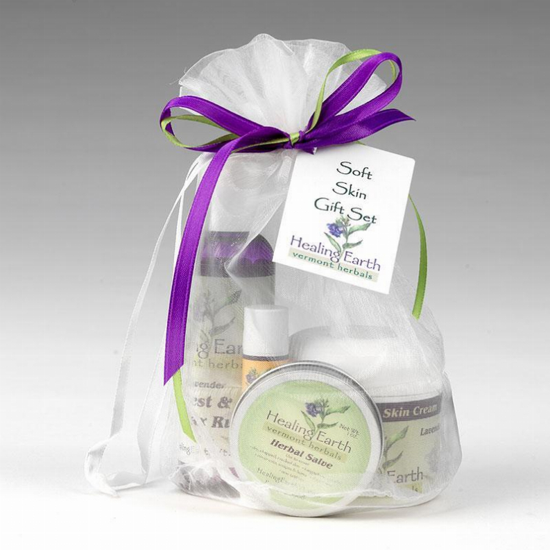 Skincare gift bag tied with purple and green ribbons, round salve tin and bottles