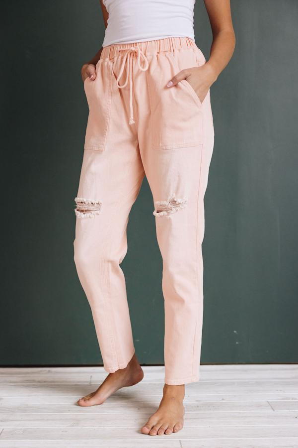 Light pink denim joggers with drawstring waistband, ripped knee details, ankle-length legs