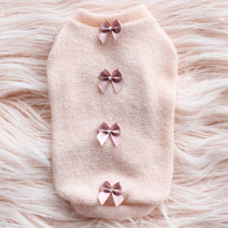 Cream fuzzy sweater with ribbed cuffs and four dusty-pink bows on the front