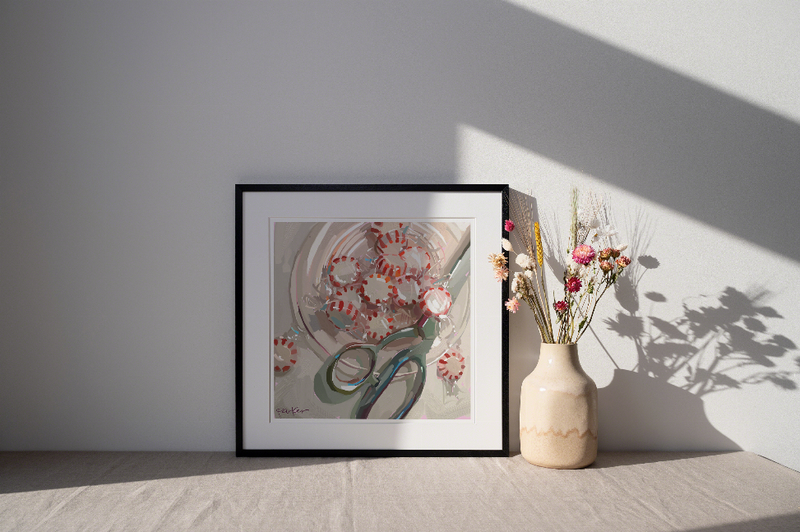 Framed abstract wall art print with red circles and green-grey shapes on a tabletop