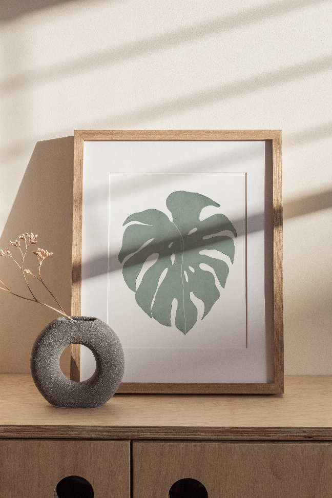 Framed monstera leaf wall print with light wood frame and muted green leaf