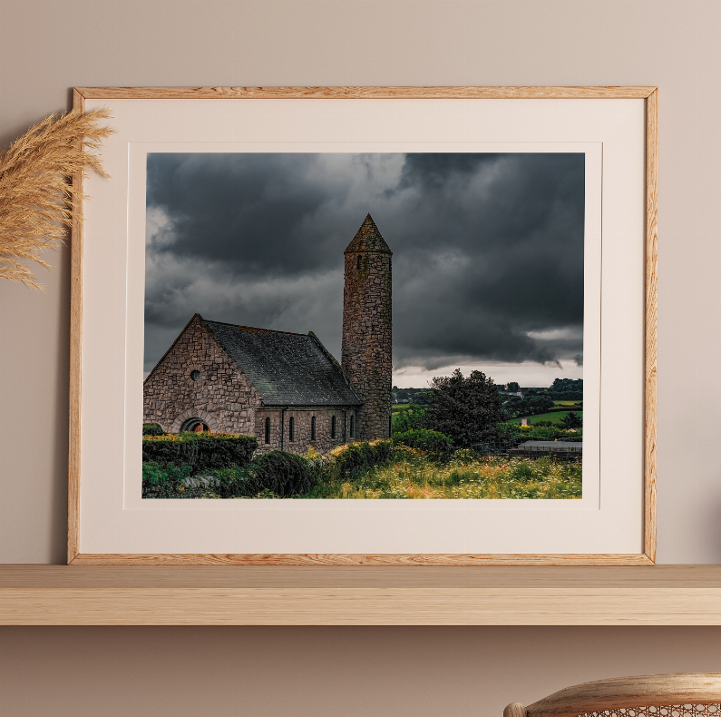 Framed landscape print of stone church and tall tower over green hills