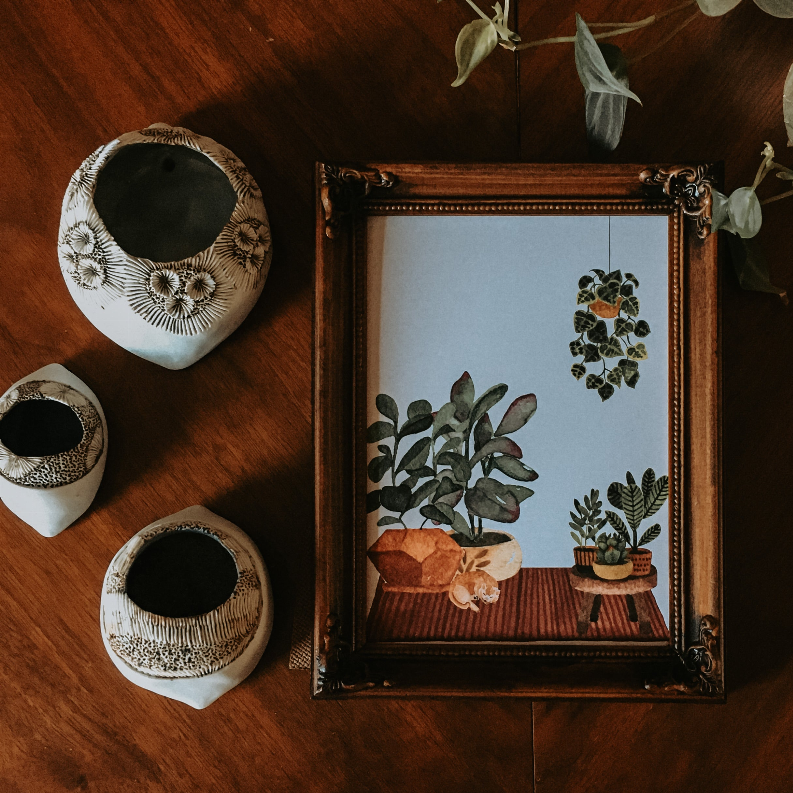 Framed botanical plant print with green foliage on a patterned table