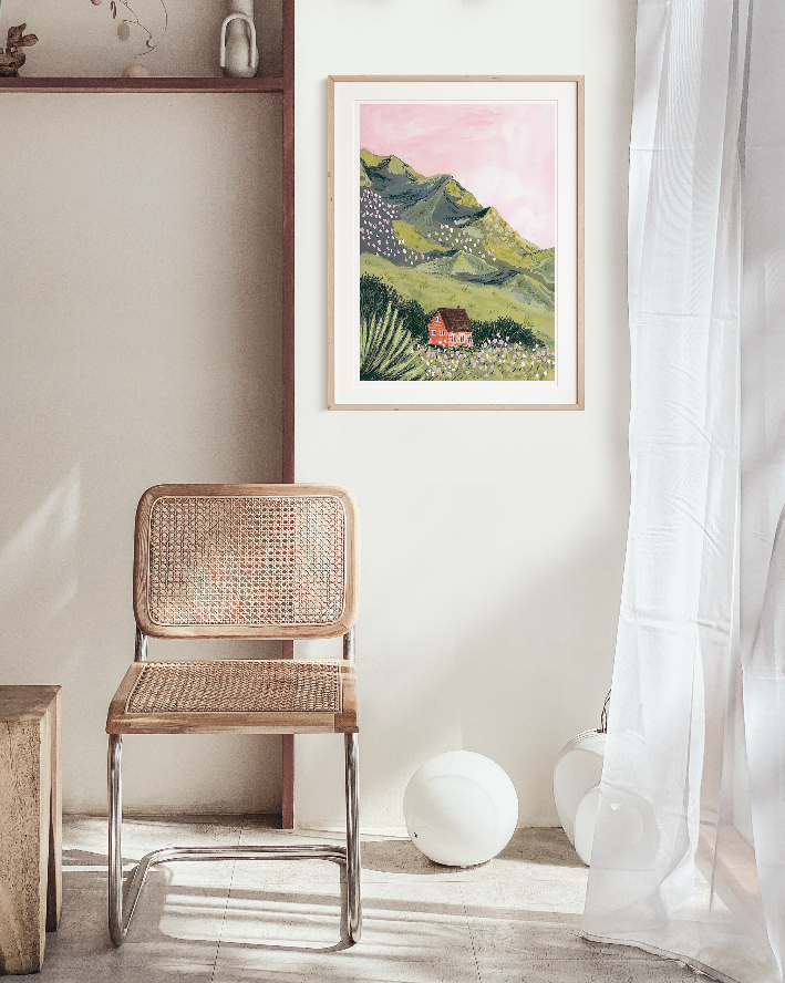 Framed mountain landscape wall art above rattan chair near white decorative balls