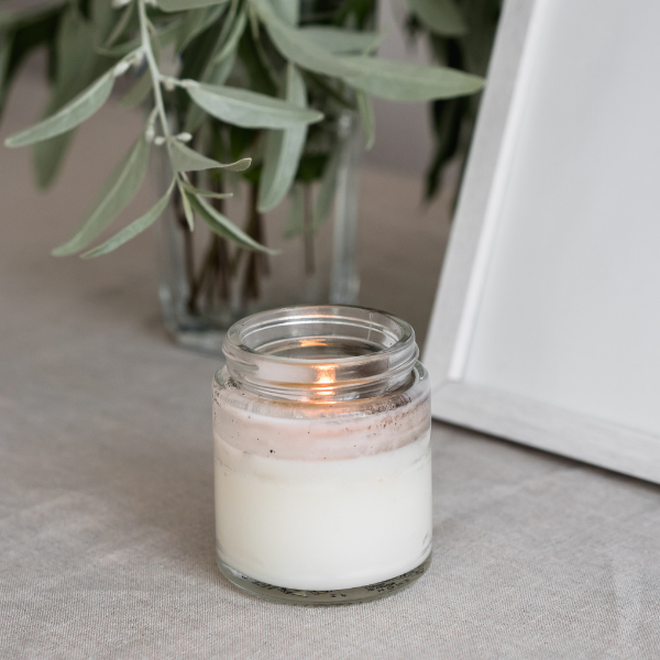 Soy candle in clear glass jar with white wax and flickering flame