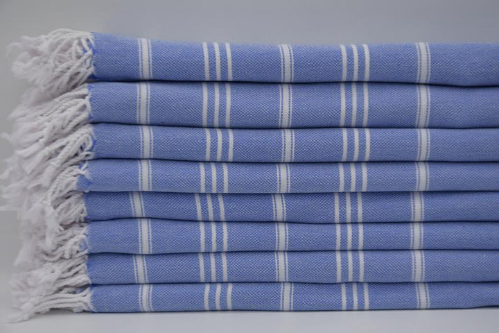 Folded blue hand towel stack with vertical white stripes and fringed towel ends.