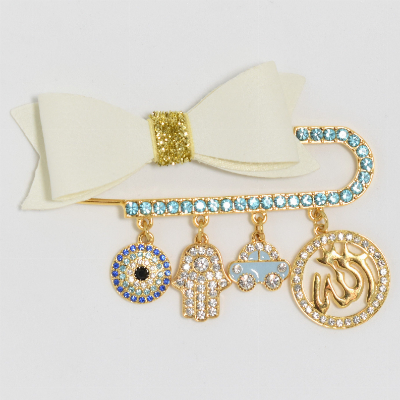 Gold-tone baby pin with cream ribbon bow, blue rhinestone bar, charm dangles