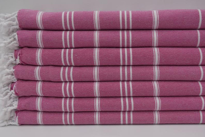 Stack of pink hand towels with white vertical stripes, terry texture and frayed edges
