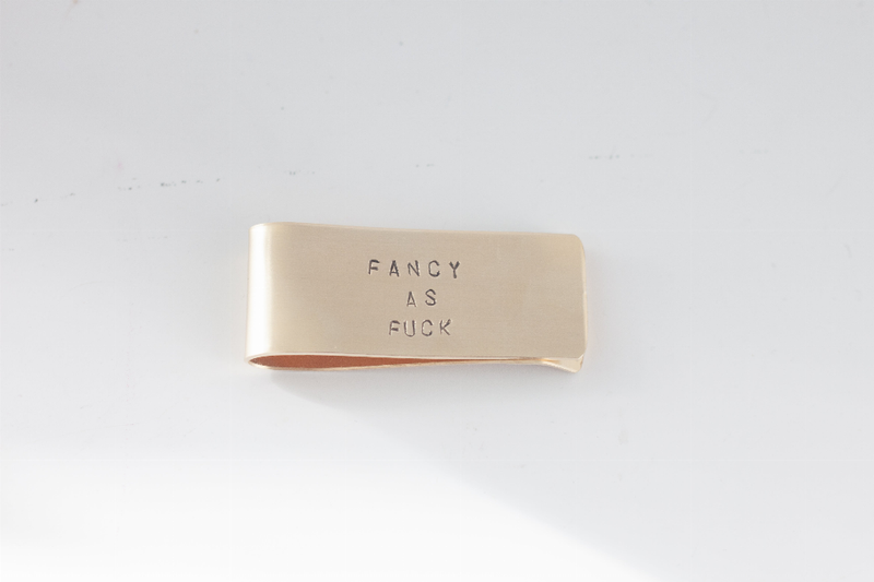Beige metal money clip with centered “FANCY AS FUCK” engraving, front view