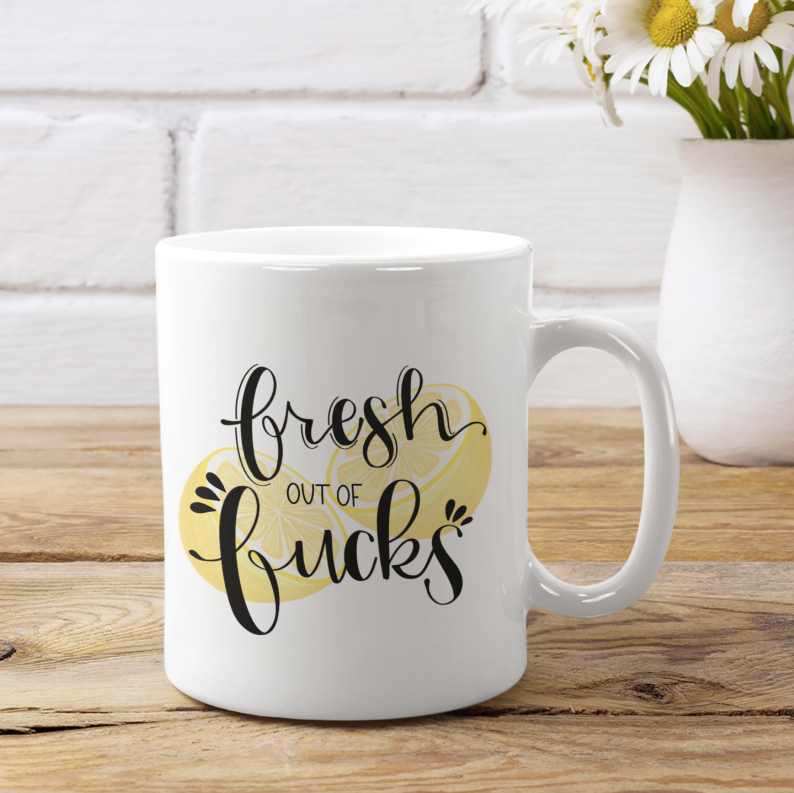 White coffee mug with 'Fresh out of Fucks' lettering and yellow heart graphic, right handle