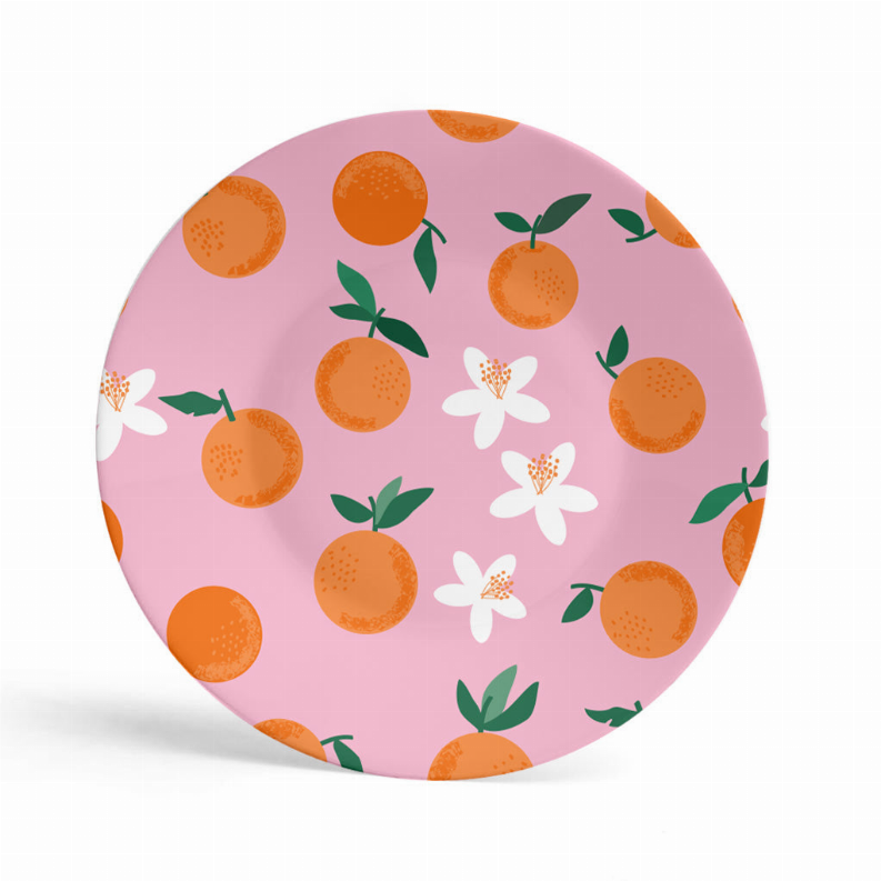 Round pink melamine plate with orange clementines, green leaves, and white flowers