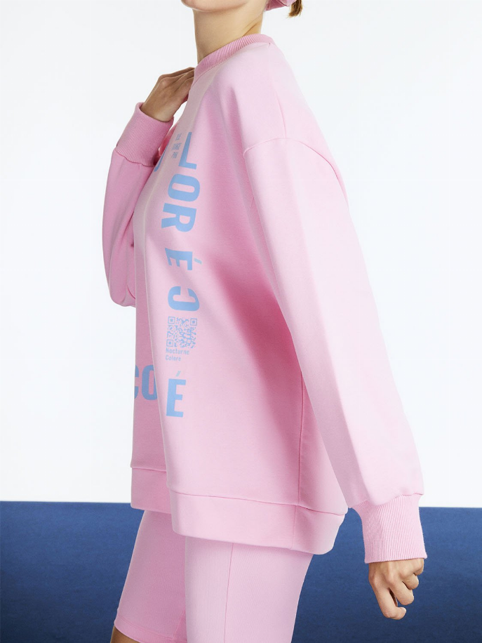 Pink oversized sweatshirt in side view with visible graphic lettering along sleeve