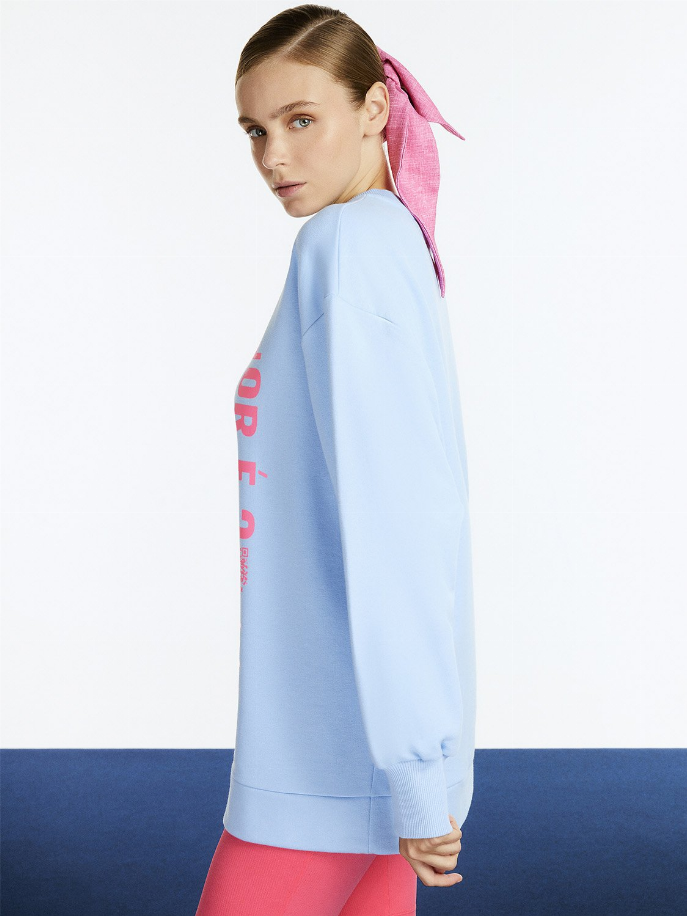 Light blue oversized crewneck sweatshirt, long sleeves, partial red graphic at sleeve