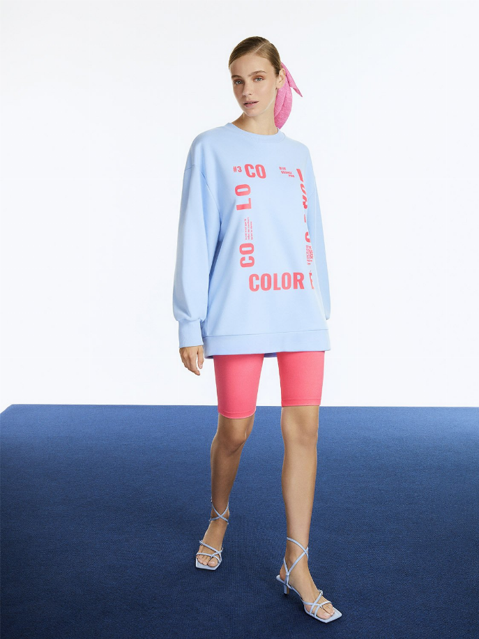 Light blue oversized crewneck sweatshirt with vertical red "COLOR" text graphic, long sleeves