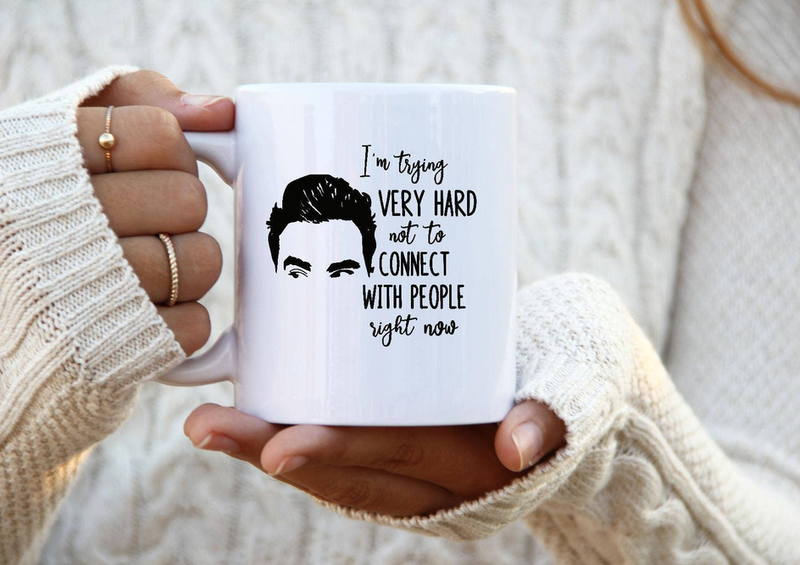 White ceramic coffee mug held in hands, featuring a black quote portrait graphic