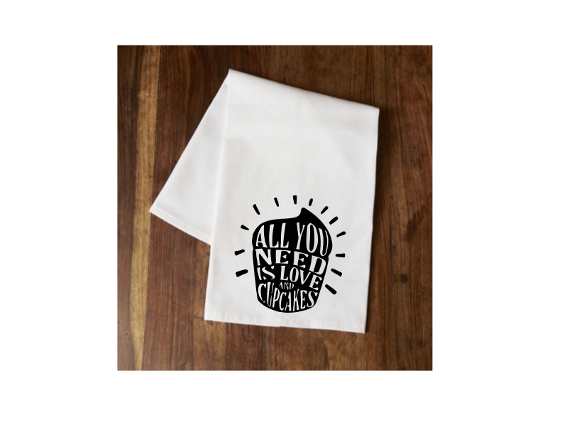 White tea towel with black text: “All you need is love” and cupcakes