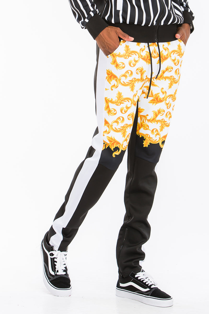 Printed track pants with orange-gold floral scroll print, black yoke, and stripe panel