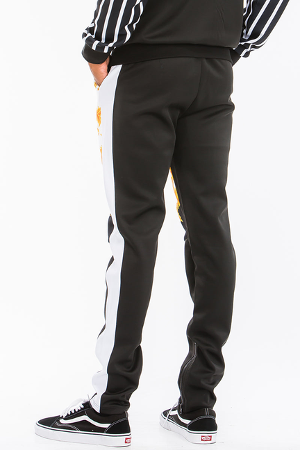 Printed track pants with black base, orange-gold scroll print, and white stripe side panels