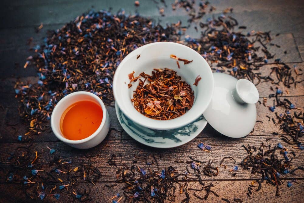 Bowl of loose black tea leaves with small dried pieces and a cup of tea