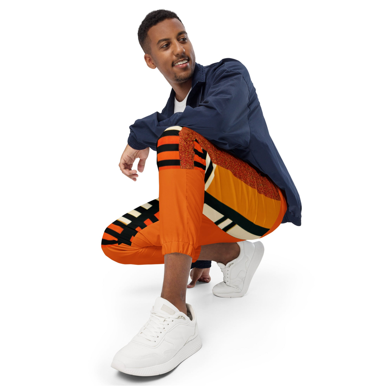 Orange printed track pants on model, striped side bands, elastic waistband, ankle cuffs.